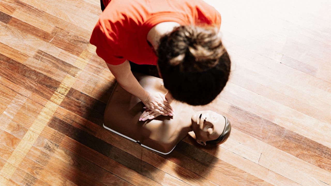 A first aid trainer demonstrating CPR chest compressions on a training manikin